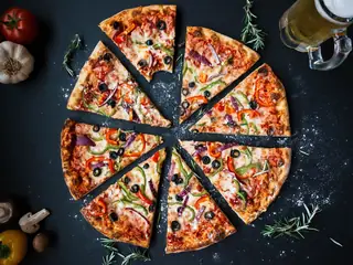 Una pizza tagliata a spicchi su un piano scuro, fra pomodori e rosmarino