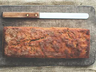 Pane in cassetta dalla crosta scura su un tagliere, col coltello