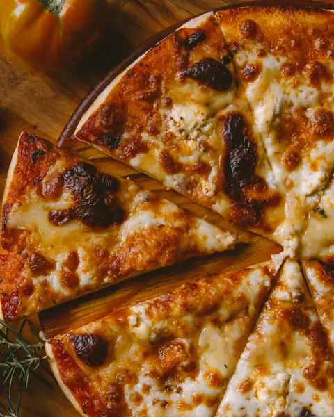Una pizza dorata tagliata a spicchi sul tagliere, con il rosmarino