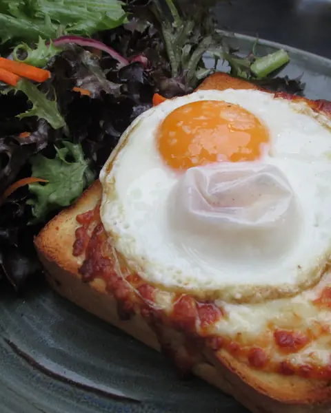 Un toast gratinato con l'uovo all'occhio di bue, accanto all'insalata
