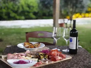 Una tavola in giardino, con un tagliere di salumi e una bottiglia di vino rosso