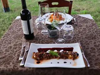 Un piatto di carne servito all’aperto, con vino rosso e calici