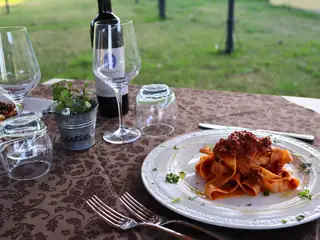 Pappardelle al ragù servite in giardino, con il vino e i calici