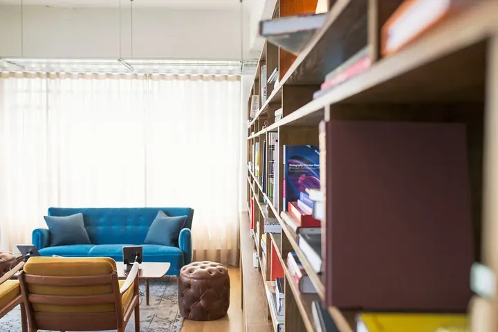Una parete attrezzata a giorno in legno, piena di libri, accanto a un divano blu