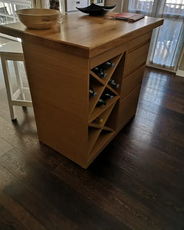 Un’isola da cucina in legno chiaro con il portabottiglie a croce su un fianco, su un parquet scuro