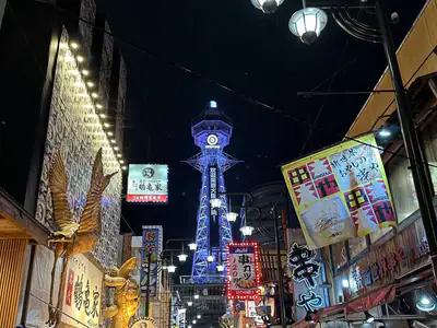 Una via di Shinsekai di notte, con la Torre Tsutenkaku illuminata in fondo