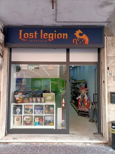 La vetrina del negozio in Via Priverno, con l'insegna «Lost legion Imperium», giochi da tavolo esposti e la sagoma di Yu-Gi-Oh! accanto alla porta
