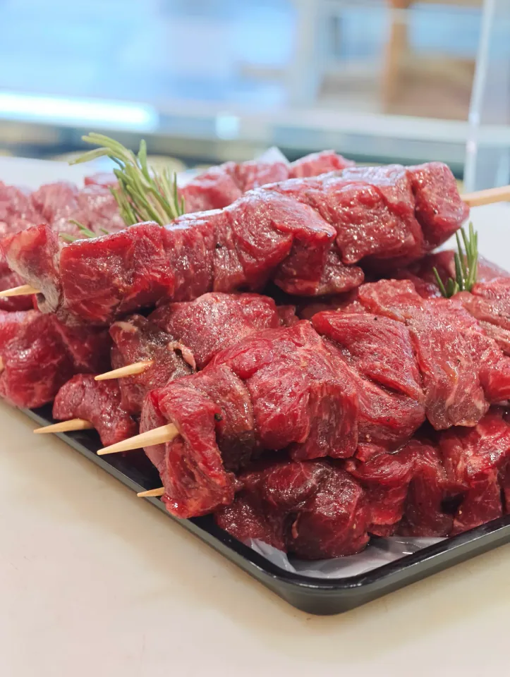 Spiedini di carne crudi con rosmarino su vassoio nero
