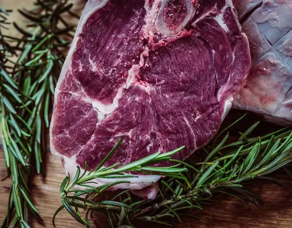 Una bistecca cruda con l'osso su un tagliere di legno, tra rametti di rosmarino