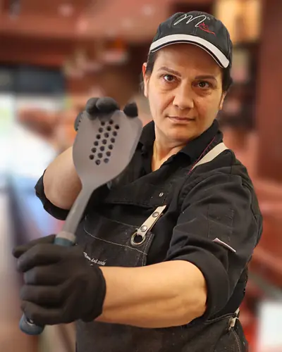 Vincenza, col cappellino della macelleria, tiene in mano una schiumarola
