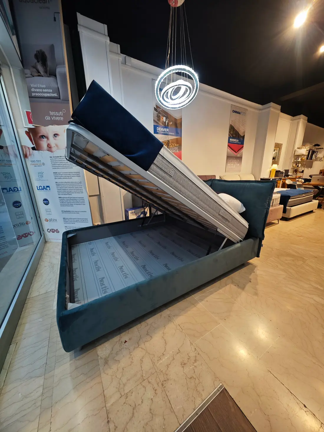 Letto contenitore in velluto blu con la rete sollevata, accanto alla vetrina