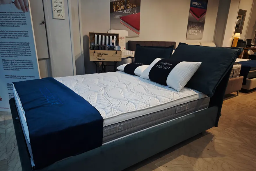 Letto imbottito con la testiera in velluto blu e il materasso bianco, nel negozio
