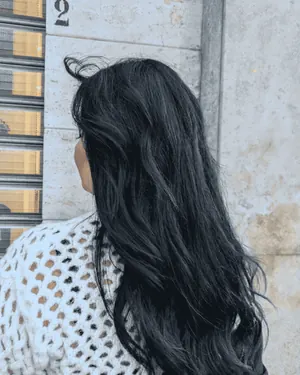 Capelli neri, lunghi e mossi, visti di spalle contro un muro
