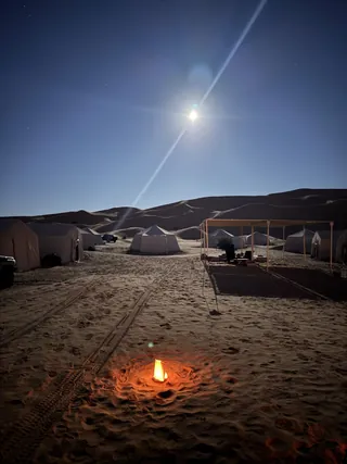 Il campo tendato nel deserto di notte, con un fuoco acceso sulla sabbia e la luna alta
