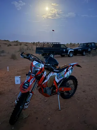 Una moto da enduro con il numero di gara, ferma nel deserto accanto a due fuoristrada