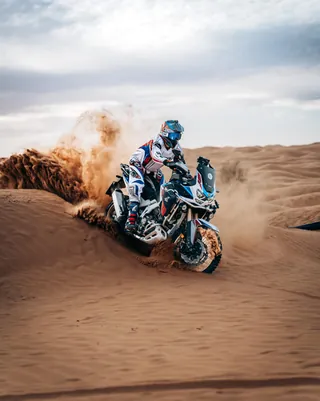 Una moto da viaggio solleva la sabbia in curva su una duna
