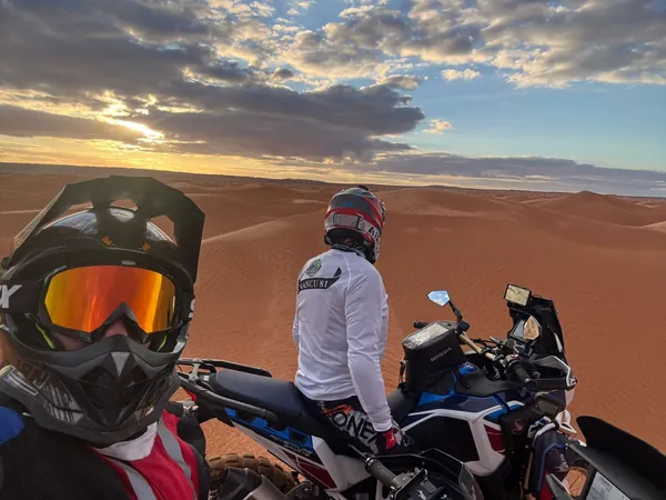 Due motociclisti con il casco da cross guardano il tramonto sulle dune