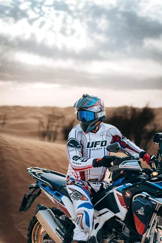 Un motociclista in tuta bianca e casco azzurro, in sella tra le dune