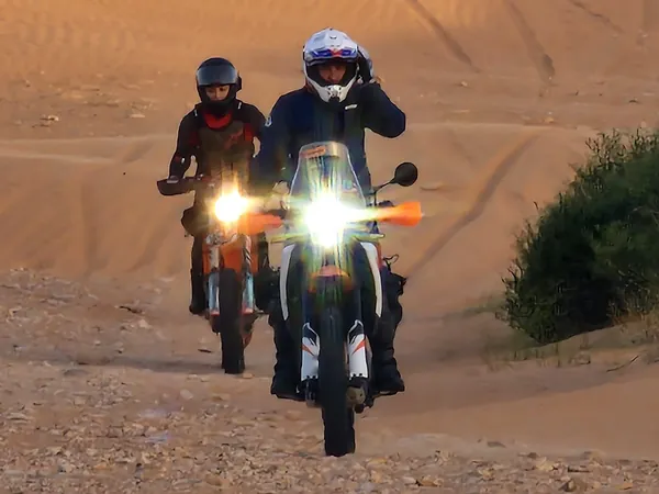 Due moto con i fari accesi avanzano sulla sabbia