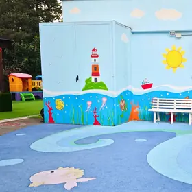 Il muro del cortile dipinto con un faro, il sole e il mare, accanto a una panchina bianca