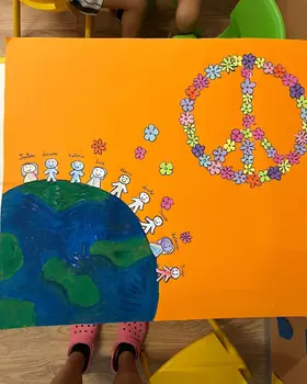 Un cartellone dei bambini con la Terra, il simbolo della pace fatto di fiori e tante figure che si tengono per mano
