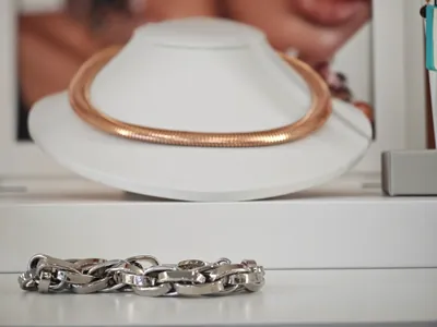Una collana a maglia in oro rosa su un busto bianco, con un bracciale d’argento davanti