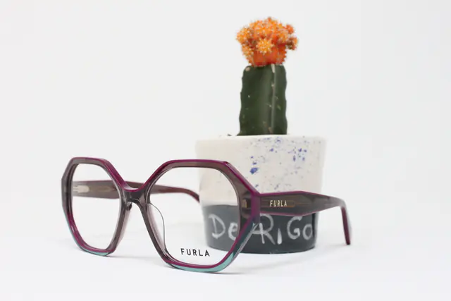 Occhiali da vista Furla viola, di forma esagonale, accanto a un piccolo cactus