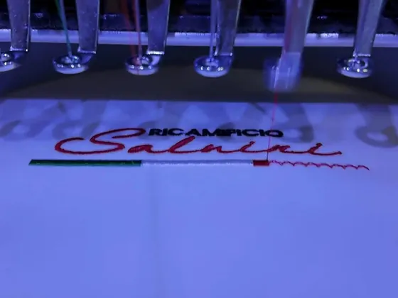 Una ricamatrice cuce la scritta Ricamificio Salvini in rosso, con il tricolore sotto