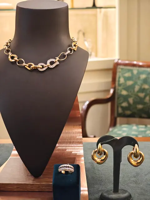 Collana a maglie in oro giallo e bianco su un busto espositore, con orecchini e anello abbinati