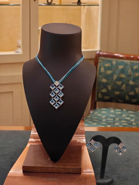 Collana con pendente a rombi di pietre azzurre su un busto espositore, con orecchini abbinati