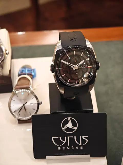 Orologio Cyrus Genève con cassa nera, esposto accanto ad altri orologi da polso