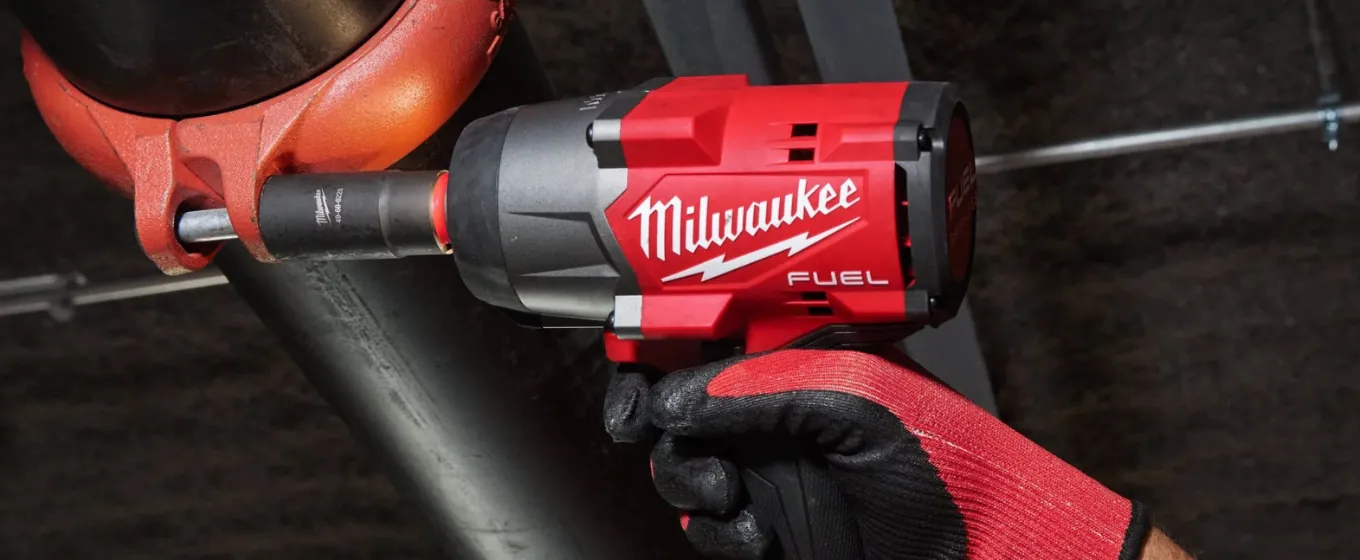Una mano col guanto da lavoro stringe un avvitatore a impulsi Milwaukee Fuel su un raccordo di tubi