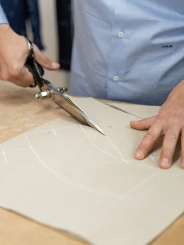 Il sarto taglia con le forbici il cartamodello tracciato col gesso sul tavolo