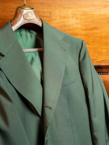 Una giacca verde su misura appesa a una gruccia di legno con il marchio della sartoria