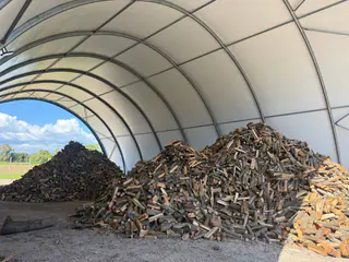 Legna spaccata sotto il tunnel coperto, con altri mucchi all’aperto sullo sfondo