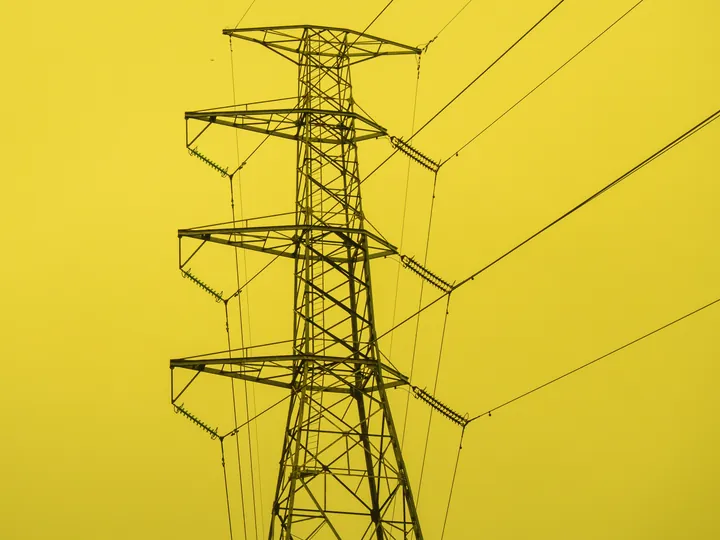 Un traliccio dell'alta tensione con i suoi cavi, contro un cielo giallo