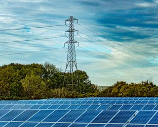 Un parco fotovoltaico al limite di un bosco, con un traliccio dell'alta tensione