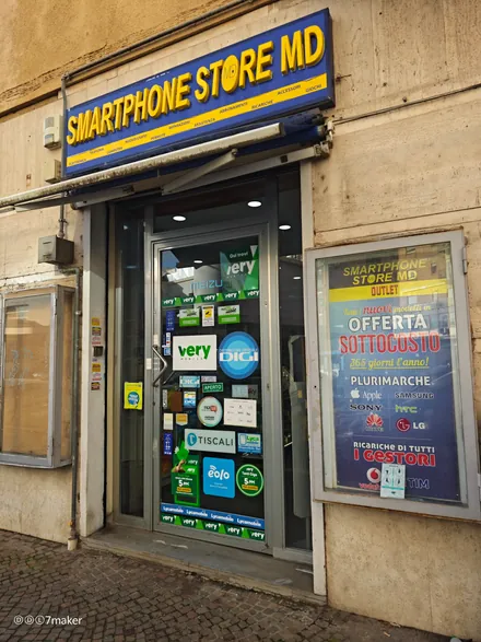 L'ingresso del punto vendita MD, con l'insegna blu e gialla «Smartphone Store MD» e la vetrina degli operatori
