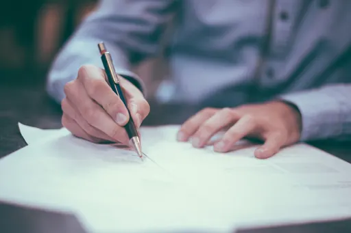Una mano firma con la penna un foglio appoggiato sul tavolo