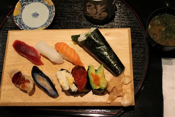 Sushi misto su un tagliere di legno: nigiri di tonno, calamaro e salmone, gunkan con uova di salmone e avocado, un temaki e lo zenzero