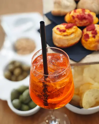 Uno spritz con ghiaccio accanto a pizzette, olive e patatine
