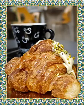 Cornetto con crema e granella di pistacchio, accanto a una tazza di caffè
