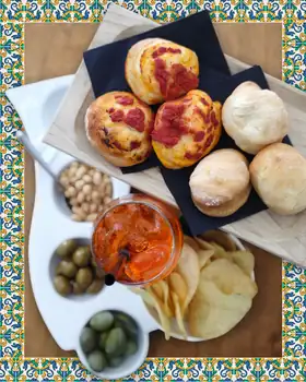 Il tagliere dell’aperitivo: pizzette, panini, arachidi, olive, patatine e uno spritz