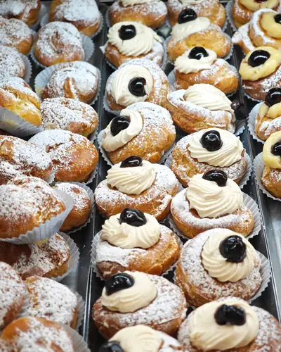 Un vassoio di zeppole con crema e amarena, spolverate di zucchero a velo