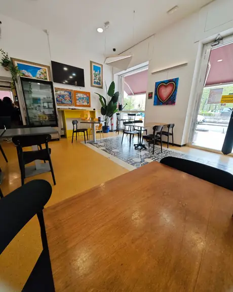La sala del bar: tavolini neri, pavimento a mattonelle decorate e quadri colorati alle pareti