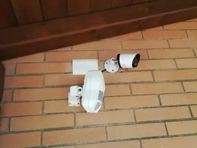 Telecamera e rilevatore da esterno su una parete di mattoni, sotto il tetto di legno