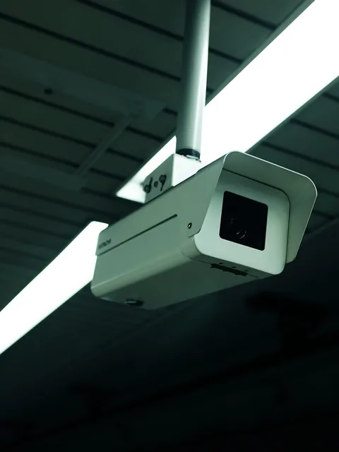 Telecamera di sorveglianza appesa al soffitto di un ambiente buio, accanto a una lampada